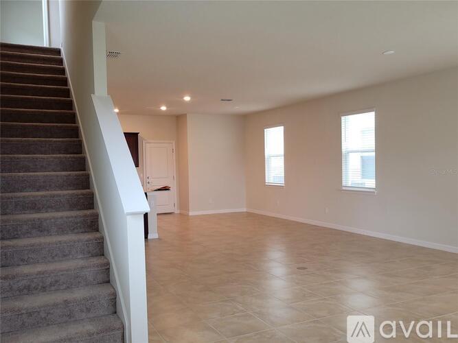 A spacious room with a staircase on the left and a door in the middle.