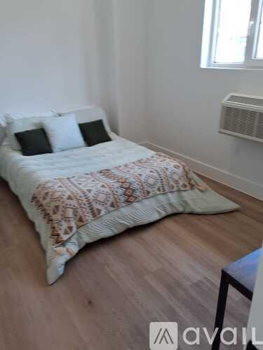 A bed with a patterned blanket and two pillows sits in a room with wooden flooring.