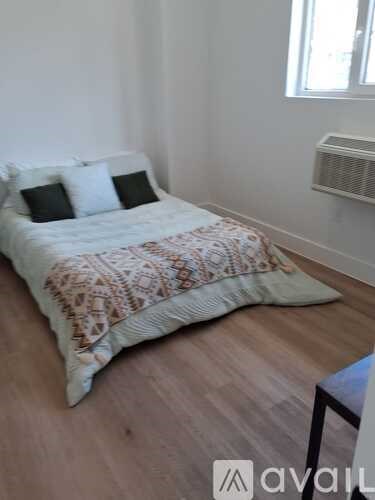 A bed with a patterned blanket and two pillows sits in a room with wooden flooring.