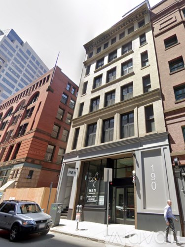 A man is walking past a building with the number 190 on it.