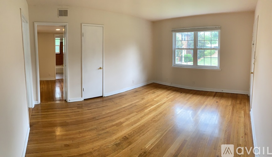 A room with wooden floors and a window with a view of a green area outside.