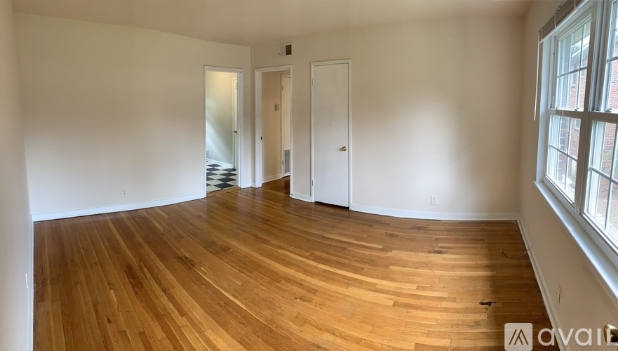 A room with wooden floors and white walls, with a door on the right and a window on the far right.