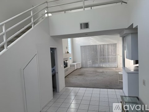 A spacious living room with a staircase on the left and a large window with curtains on the right.