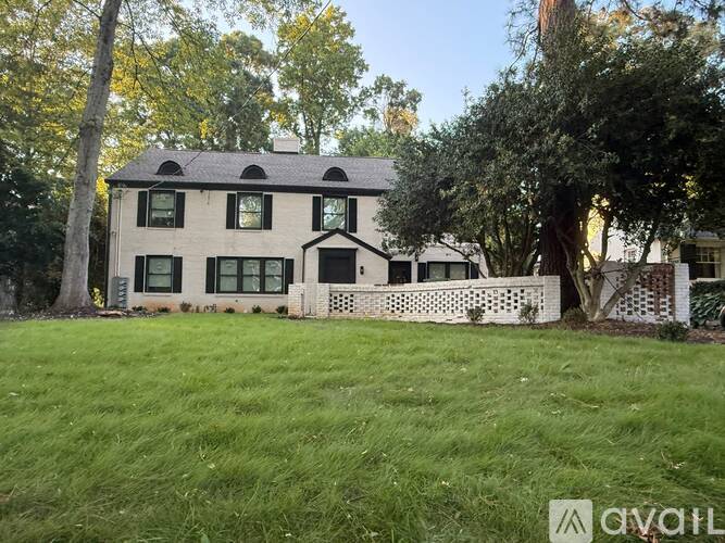 A house with a white facade and a black roof is surrounded by a well-maintained lawn and trees.