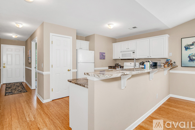 A kitchen with white cabinets and appliances, a rug on the floor, and a painting on the wall.