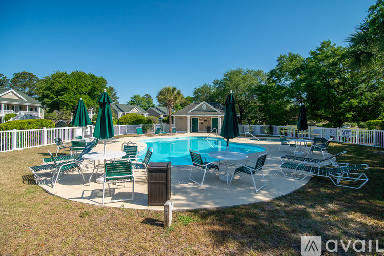 A pool surrounded by chairs and umbrellas with a house in the background.