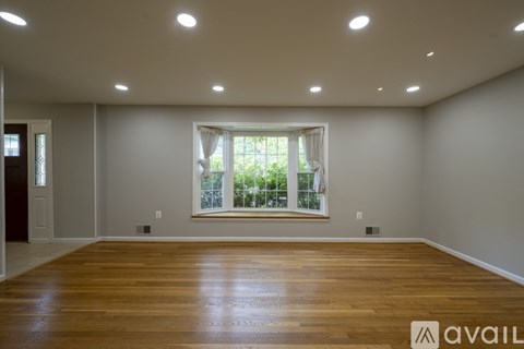 A spacious room with wooden flooring and a window with white curtains.
