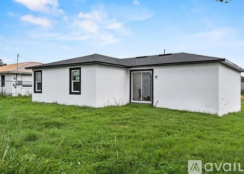 A small white house with a black roof is situated in a grassy area.