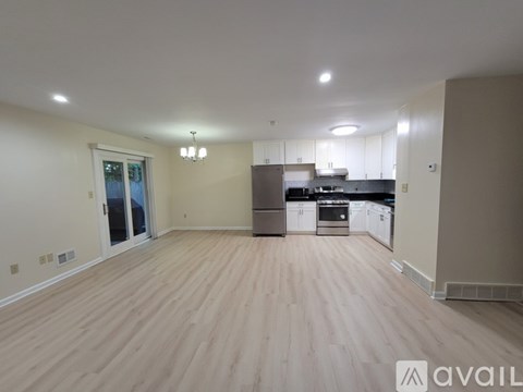 A spacious living room with hardwood floors and a kitchen area in the background.
