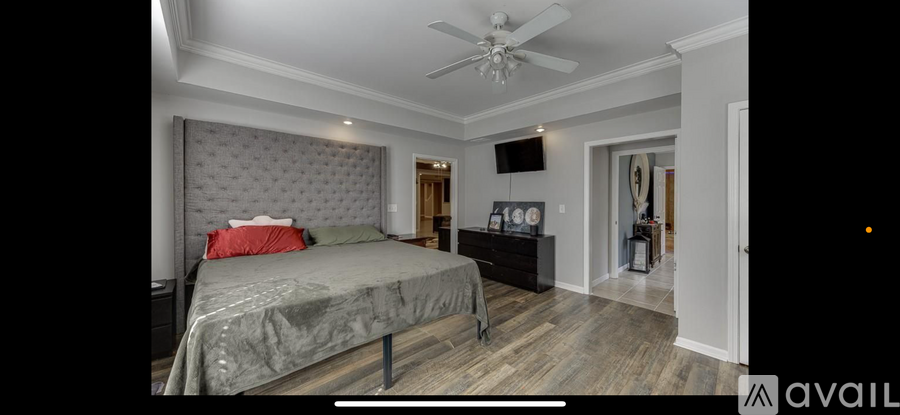 A bedroom with a bed, a ceiling fan, and a TV mounted on the wall.