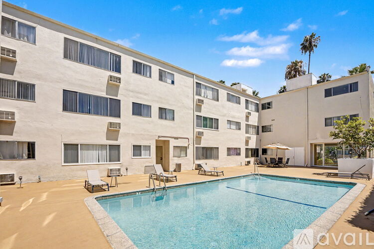 A large swimming pool is surrounded by lounge chairs in front of a building.