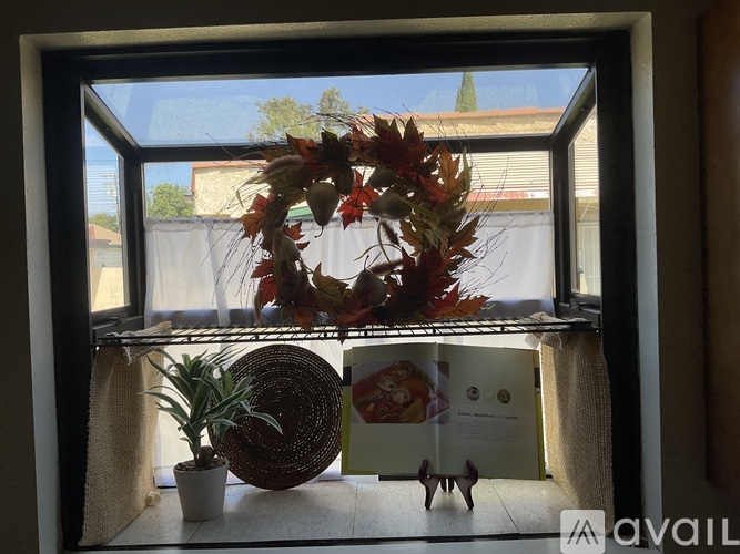 A wreath of leaves sits on a windowsill next to a potted plant and a small figurine.