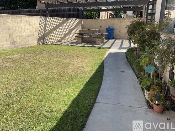 A concrete walkway leads to a small wooden table in a backyard.