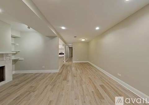 A spacious room with wooden flooring and a fireplace on the left side.