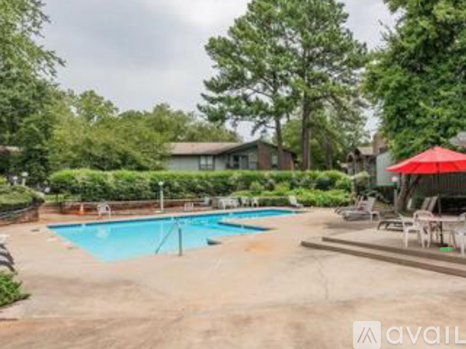 A pool surrounded by trees and a patio with chairs and an umbrella.