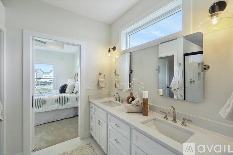 A bathroom with a large mirror, a sink, and a bedroom with a bed and a window.