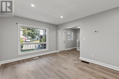 A spacious room with a large window and wooden flooring.