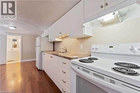 A white stove is in a kitchen with white cabinets and a white fridge.