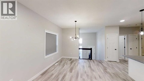A spacious room with a large window, hardwood floors, and a chandelier.