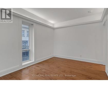 A room with wooden flooring and white walls, with a window showing a view of a building.