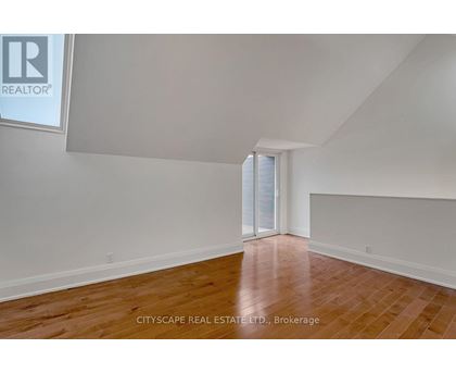 A spacious room with wooden flooring and a sliding glass door.