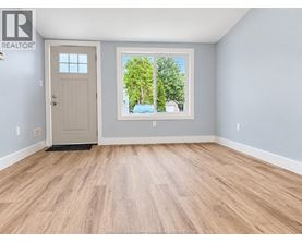 A room with a wooden floor and a door leading to a balcony with trees visible outside.