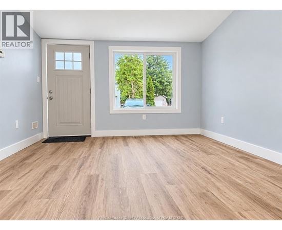 A room with a wooden floor and a door leading to a balcony with trees visible outside.