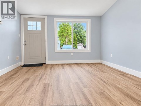 A room with a wooden floor and a door leading to a balcony with trees visible outside.