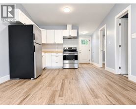 A kitchen with a black fridge, white cabinets, and a wooden floor.