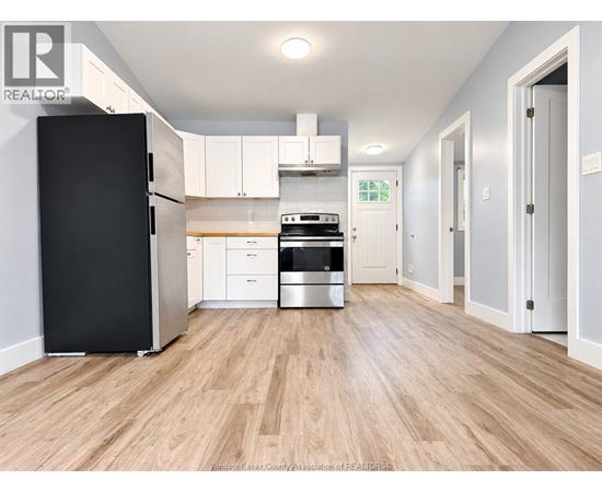 A kitchen with a black fridge, white cabinets, and a wooden floor.