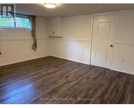 A room with wooden flooring and white walls, with a window on the left side.