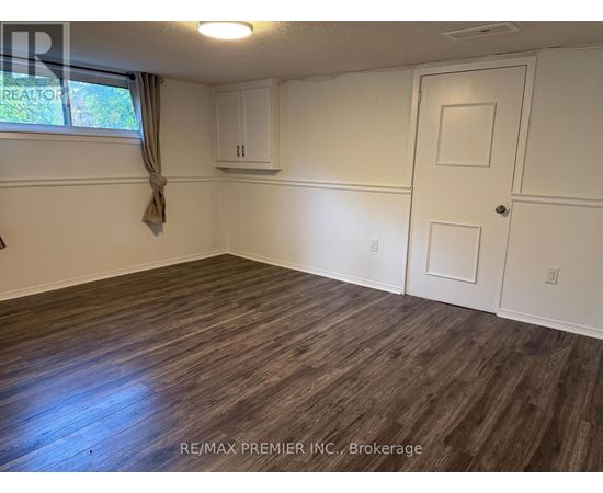 A room with wooden flooring and white walls, with a window on the left side.