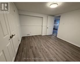 A room with wood flooring and white walls, with a door on the left and a window on the right.
