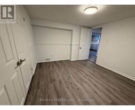 A room with wood flooring and white walls, with a door on the left and a window on the right.