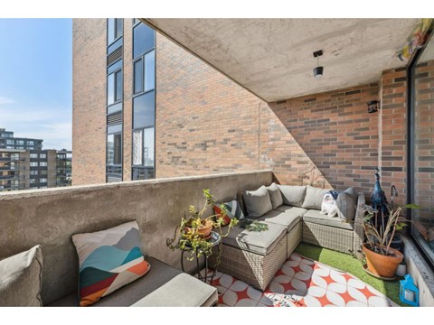 A balcony with a couch, pillows, and plants.