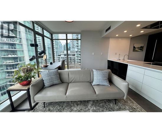 A grey couch with two pillows sits in a modern living room with a view of a cityscape.