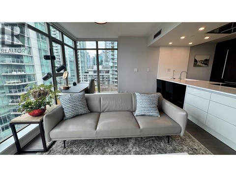 A grey couch with two pillows sits in a modern living room with a view of a cityscape.