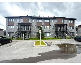 A large building with a grey and brown exterior and a small green area in front.