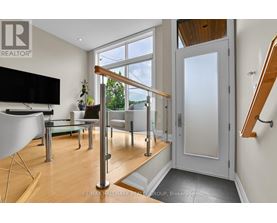 A living room with a television, a glass table, a sofa, and a staircase.