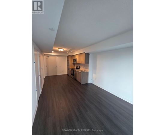 A spacious room with wooden flooring and a kitchen area in the background.