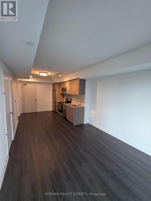 A spacious room with wooden flooring and a kitchen area in the background.