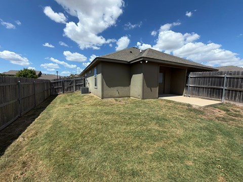 A house with a brown roof and a grey exterior is surrounded by a wooden fence.