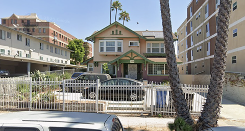 A house with a green roof is surrounded by a white fence and has a car parked in front.