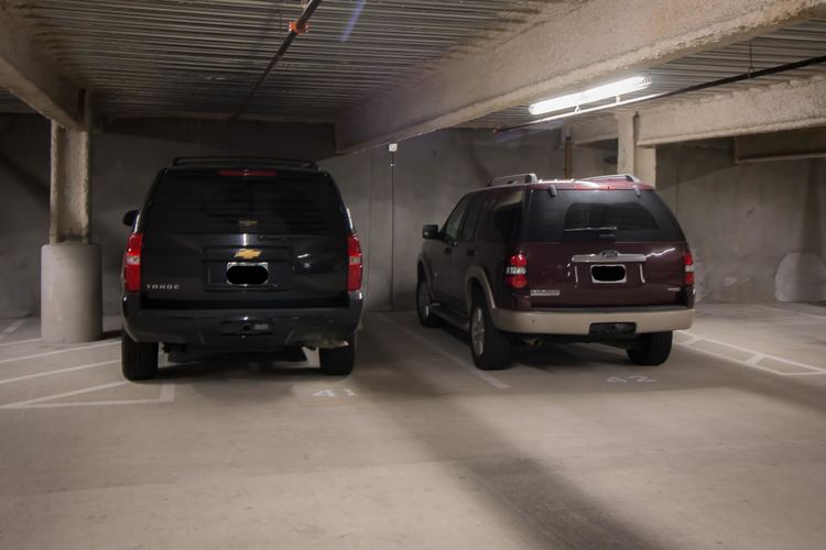 Two black SUVs are parked in a dimly lit parking garage.