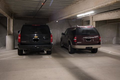 Two black SUVs are parked in a dimly lit parking garage.