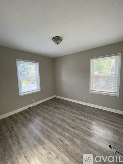 A room with wooden flooring and two windows.
