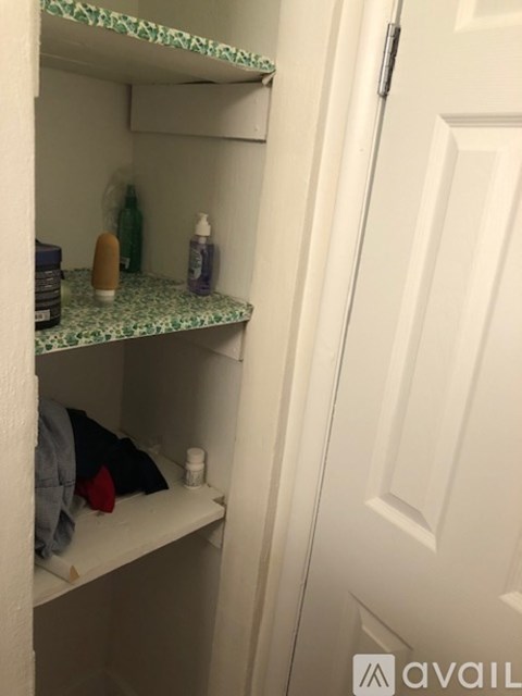 A white door is to the right of a shelf with a green bottle and other items on it.