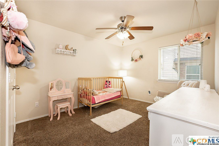 A baby's room with a crib, a dresser, and a fan.