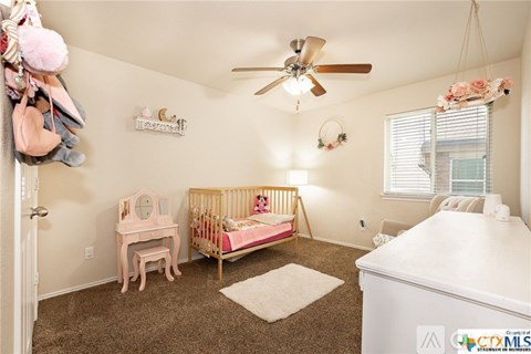A baby's room with a crib, a dresser, and a fan.