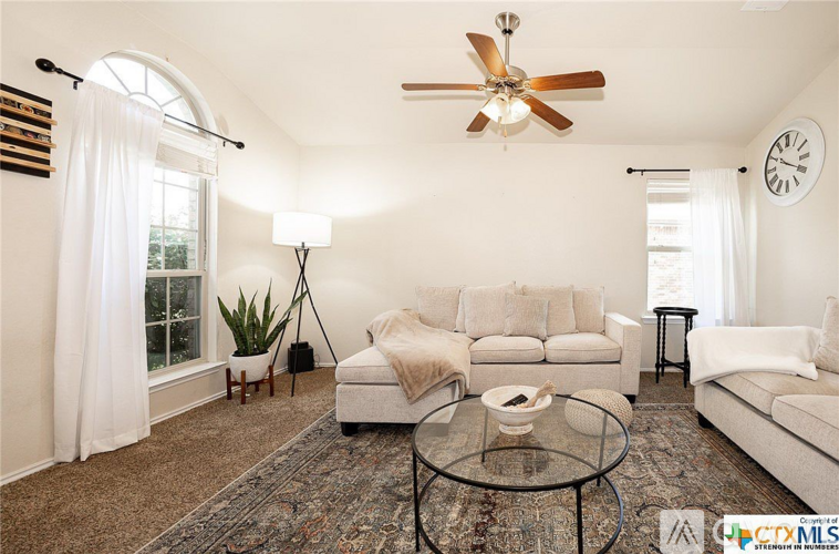 A living room with a white couch, a rug, a glass table, and a ceiling fan.